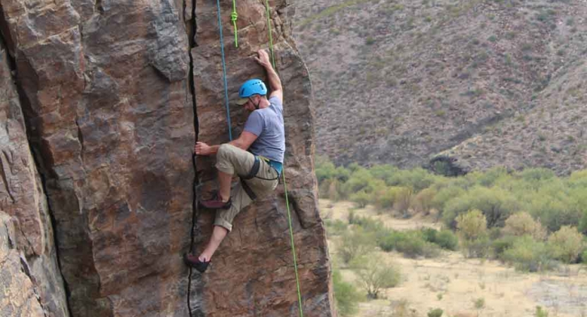 a gap year student rock climbs above a desert landscape in texas